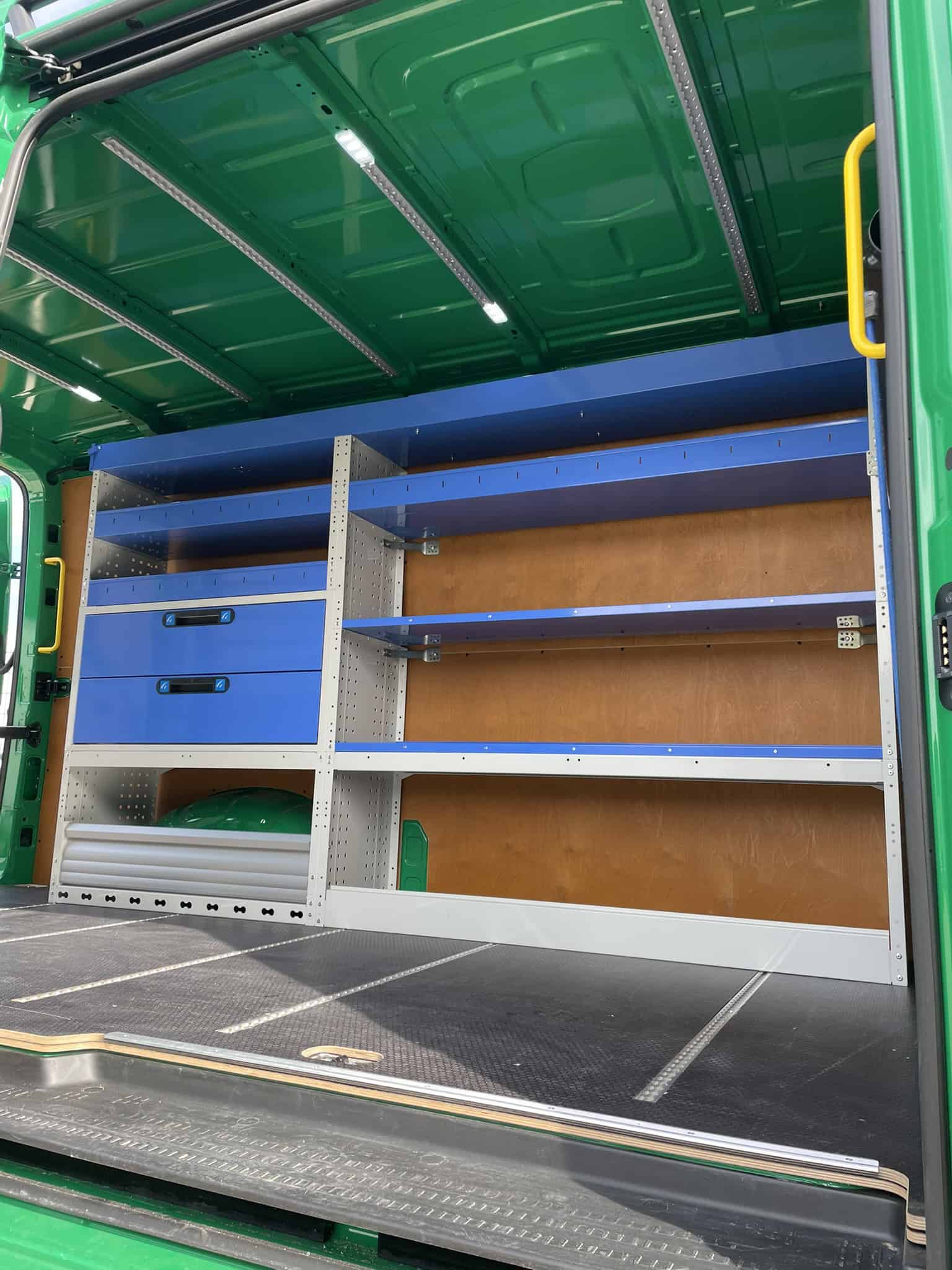 Kleurrijke bedrijfswageninrichting met geperforeerde metalen kasten en houten planken, perfect voor het organiseren van gereedschap en materialen in bedrijfswagens.