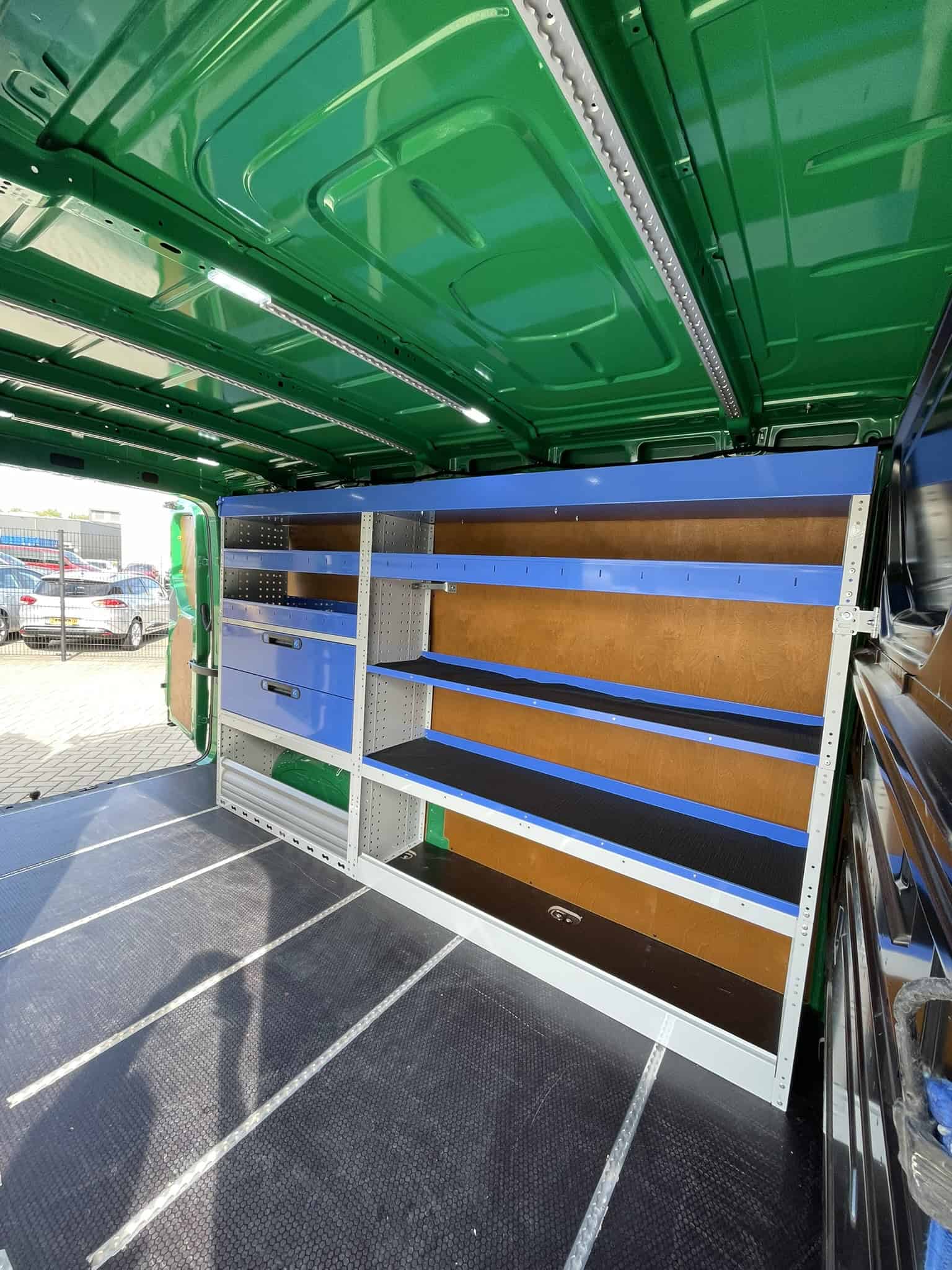 Gestuurde bedrijfswageninrichting met opbergsystemen, werkbanken en verzamelbakken in een groene bedrijfsbus voor vakmanschap en efficiëntie.