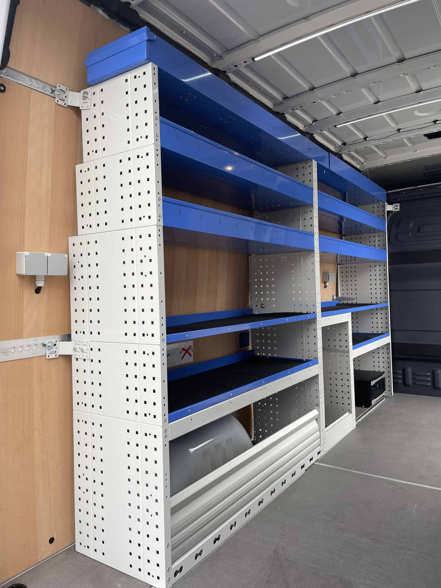 Robuuste bedrijfswageninrichting met blauwe en witte stalen planken en legborden in laadruimte, ideaal voor organisatie en opslag van gereedschap en materialen.