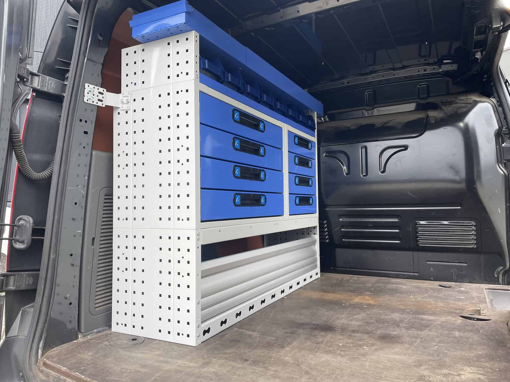 Zwaar uitgevoerde bedrijfswageninrichting met blauwe opbergkasten en gereedschapsrekken in de laadruimte van een bedrijfswagen, ontworpen voor efficiënte werkplaatsorganisatie en optimale benutting van de laadruimte.