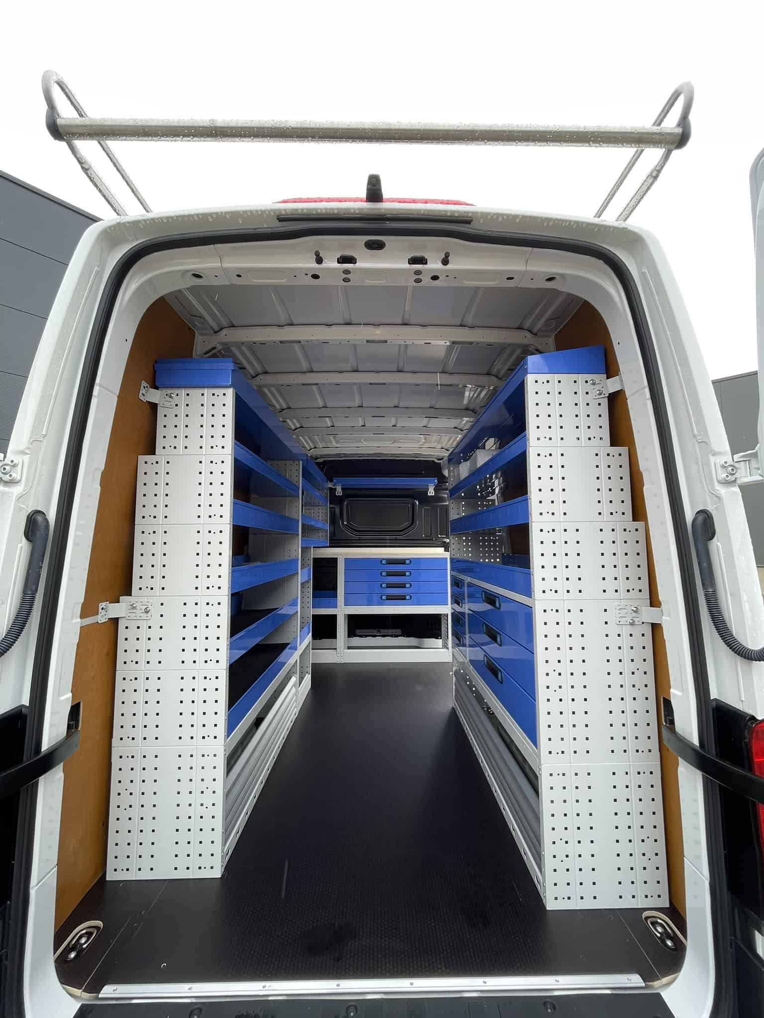 Interieur van een bedrijfswagen met georganiseerde blauwe en witte opbergrekken voor gereedschap en onderdelen, ideaal voor bedrijfswageninrichting en werkplaatsorganisatie.