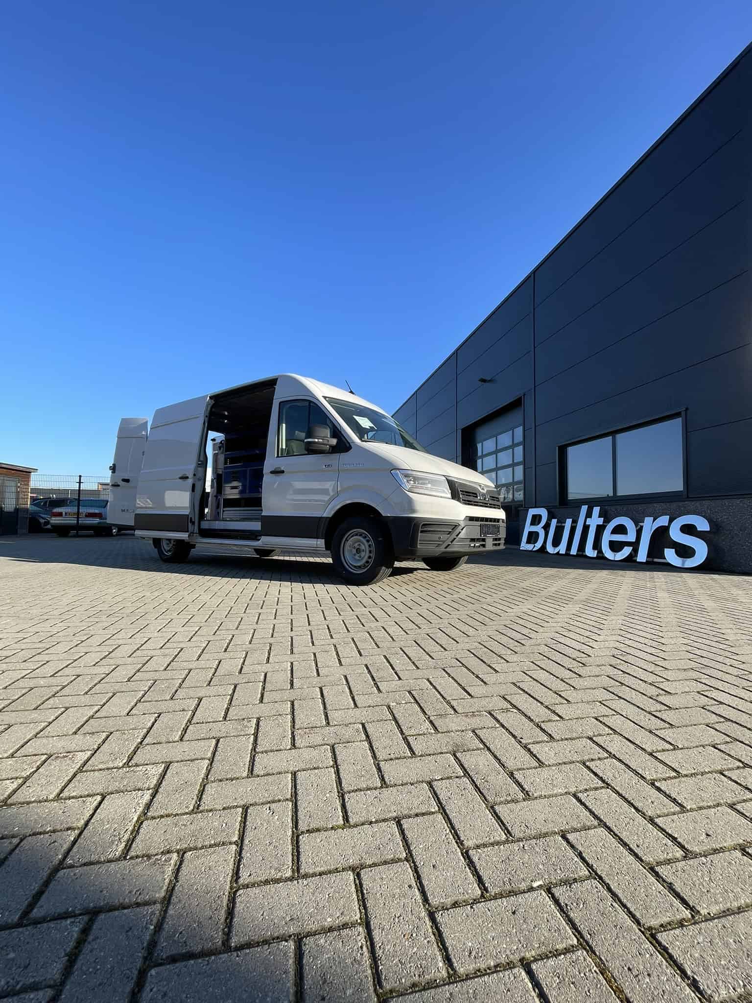 Bedrijfswagen met op maat gemaakte inrichting voor efficiënt transport en logistiek, geparkeerd voor een modern bedrijfsgebouw met de naam 'Bulters'.