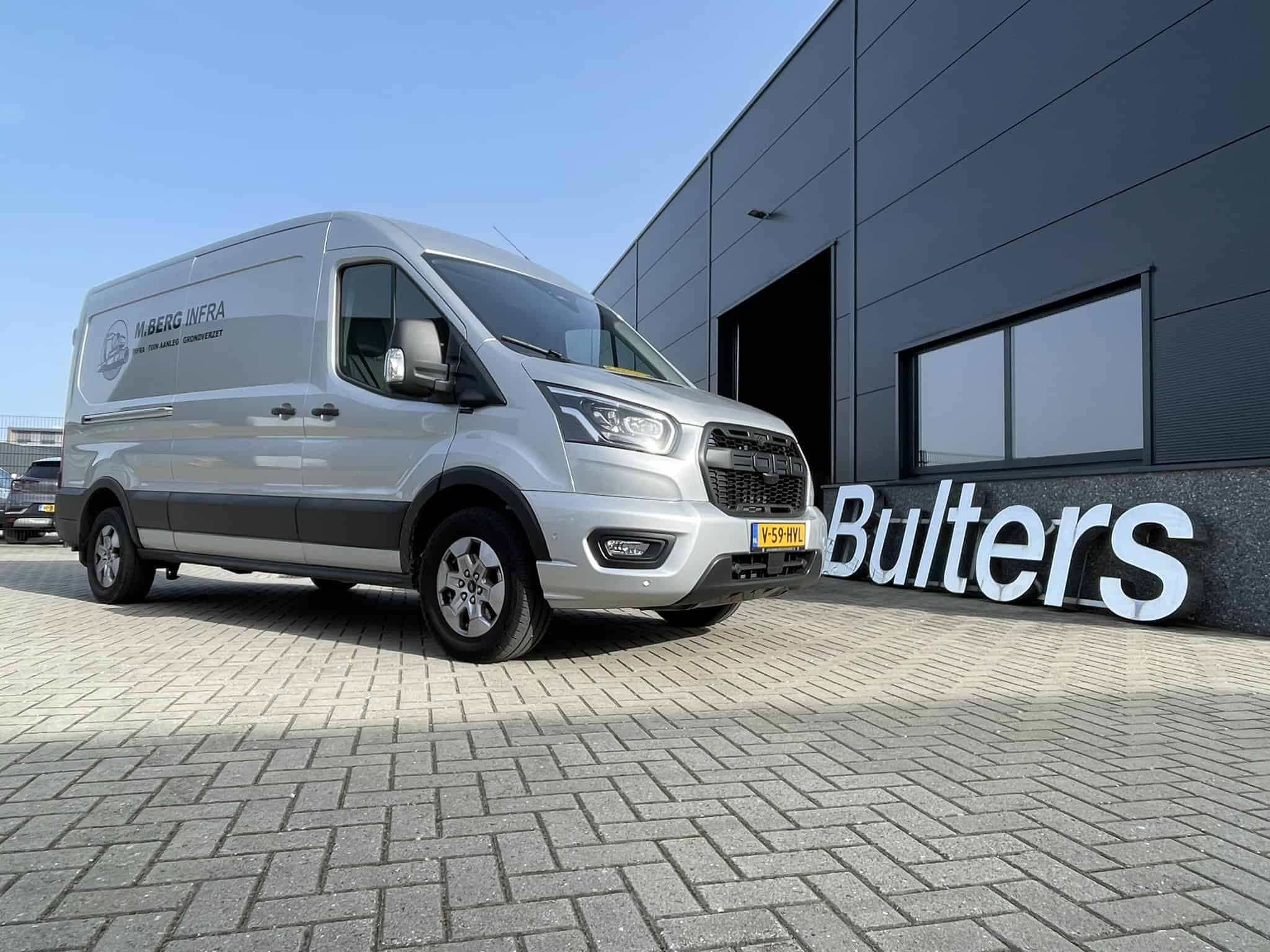 Bedrijfswagen met bedrijfslogo voor bedrijfsinrichting, geparkeerd voor een modern bedrijfspand met de naam 'Bulters' op de gevel.