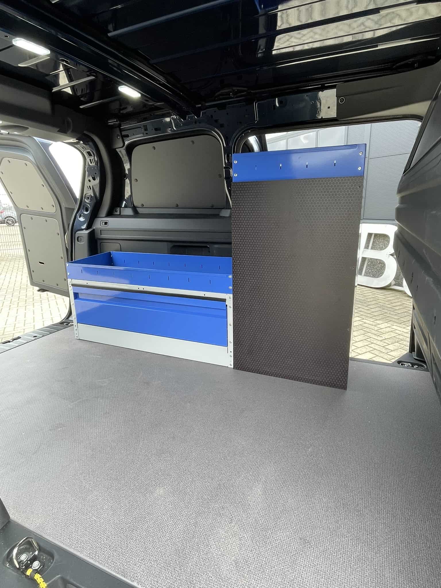 Binnenkant van een bedrijfswagen met blauwe opbergkasten en een zwart werkblad, ideaal voor professioneel gebruik.