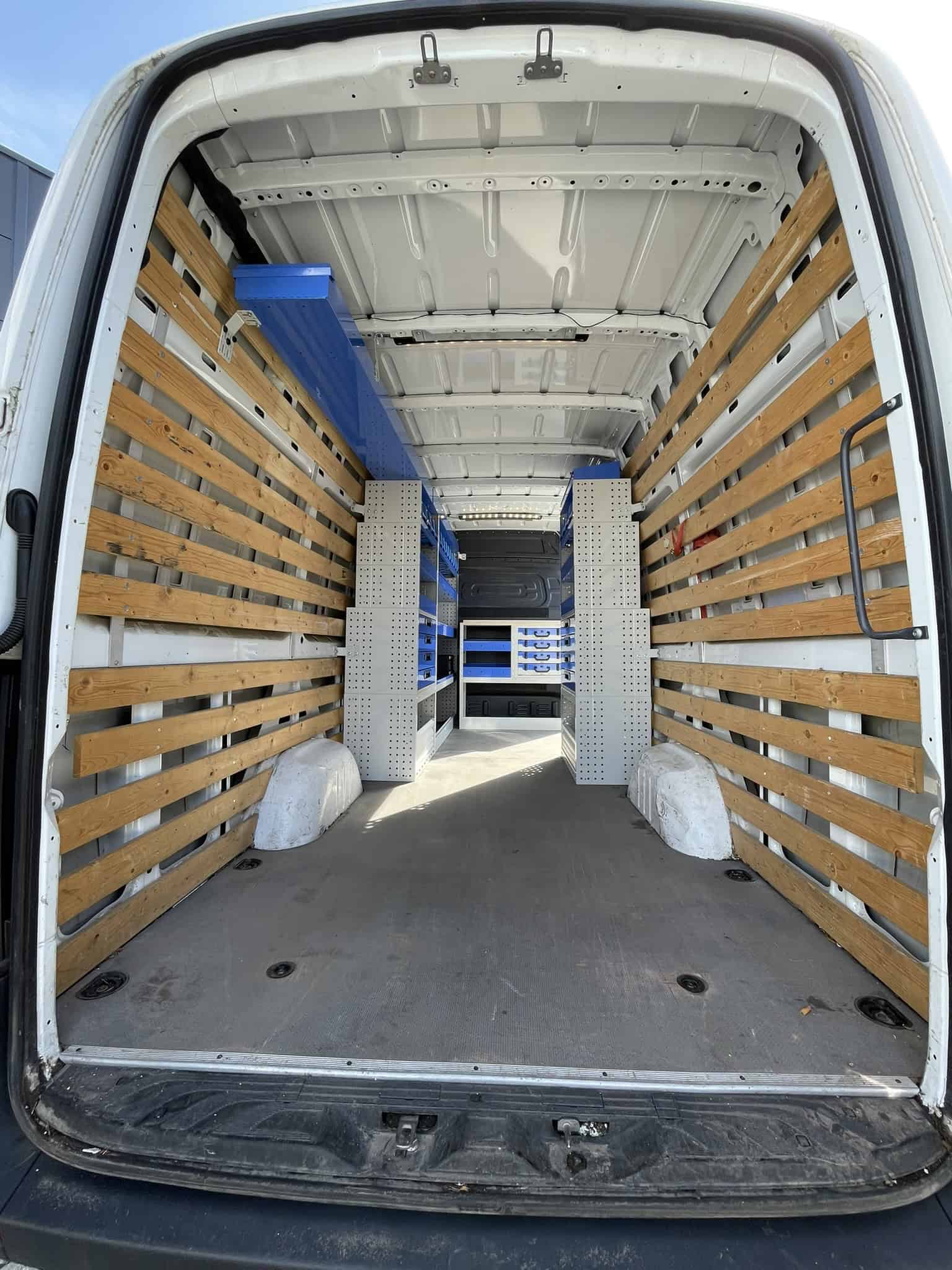 Interieur van een bedrijfswagen met houten zijwanden en opbergsystemen voor efficiënte opslag en transport.