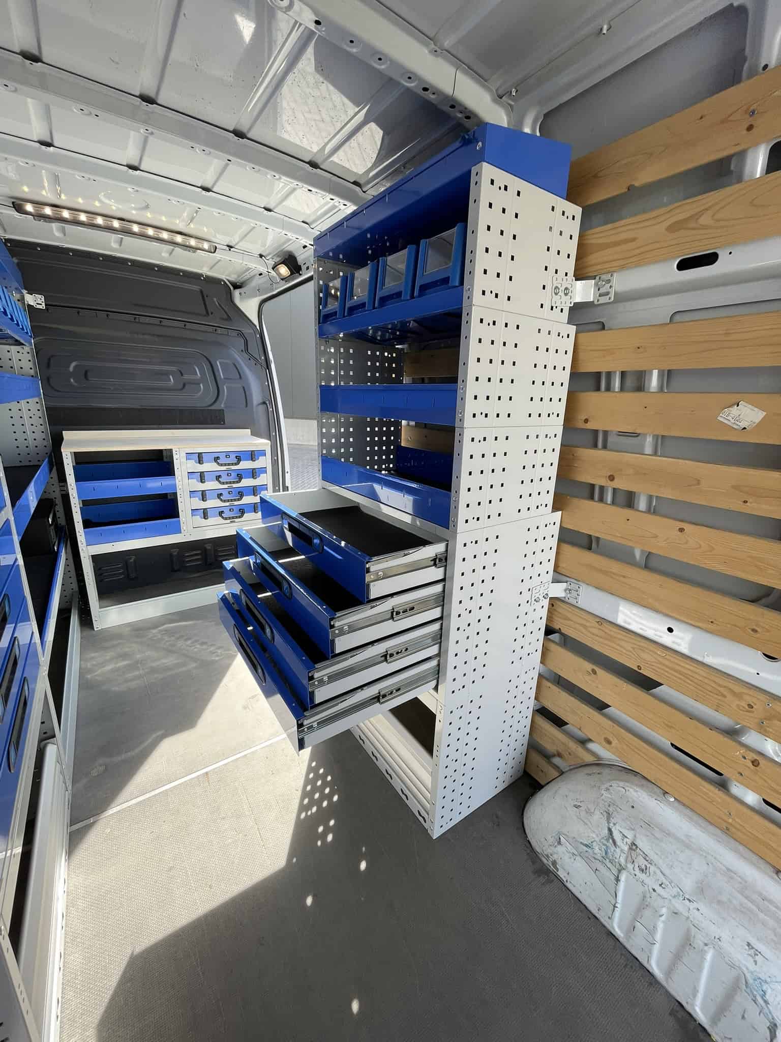 Binnenkant van een bedrijfswagen met op maat gemaakte blauwe en witte opbergkasten en lades voor gereedschap en materialen.
