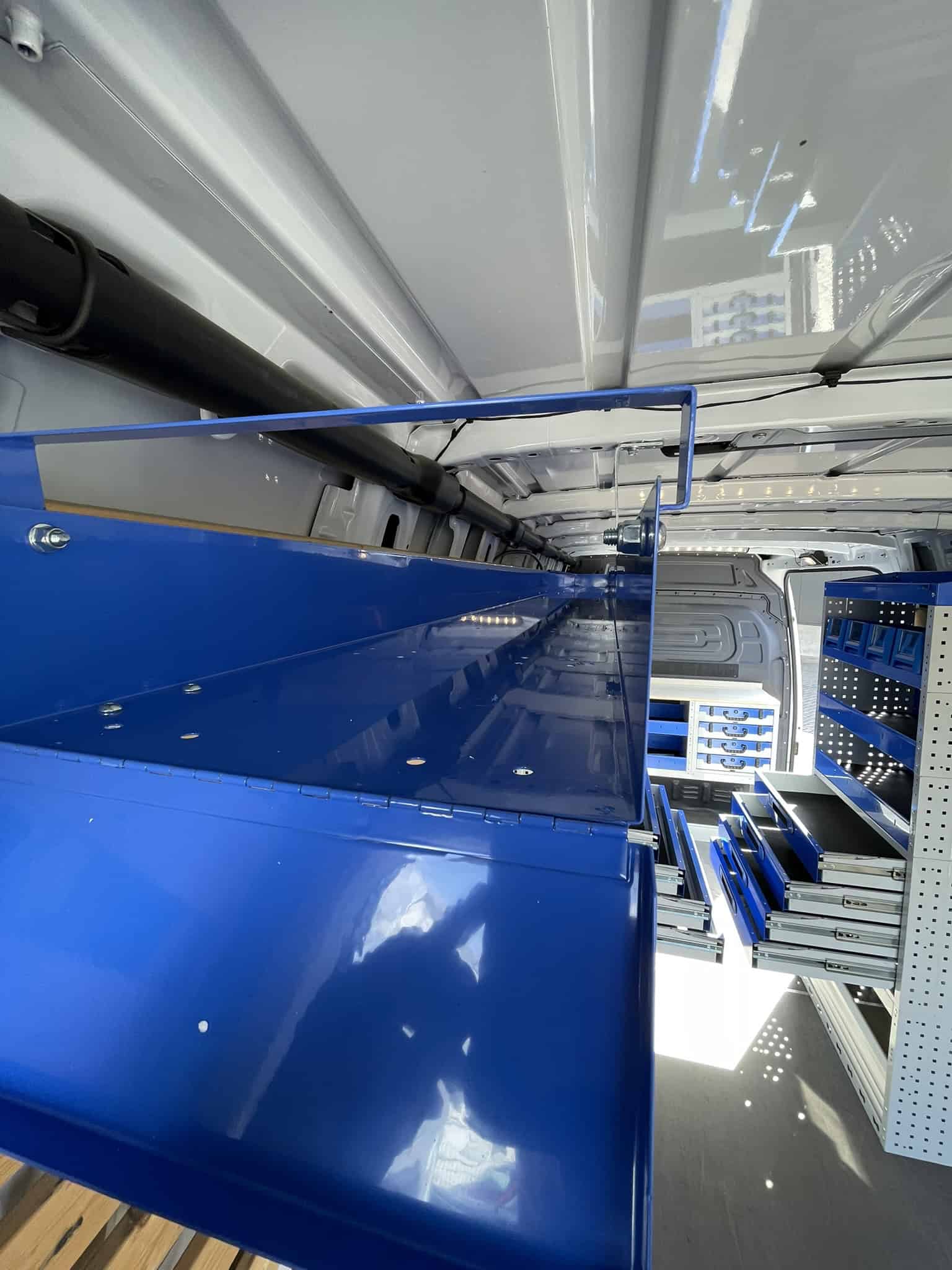Binnenkant van een bedrijfswagen met blauwe opbergkasten en werkruimte voor professionele werkzaamheden.