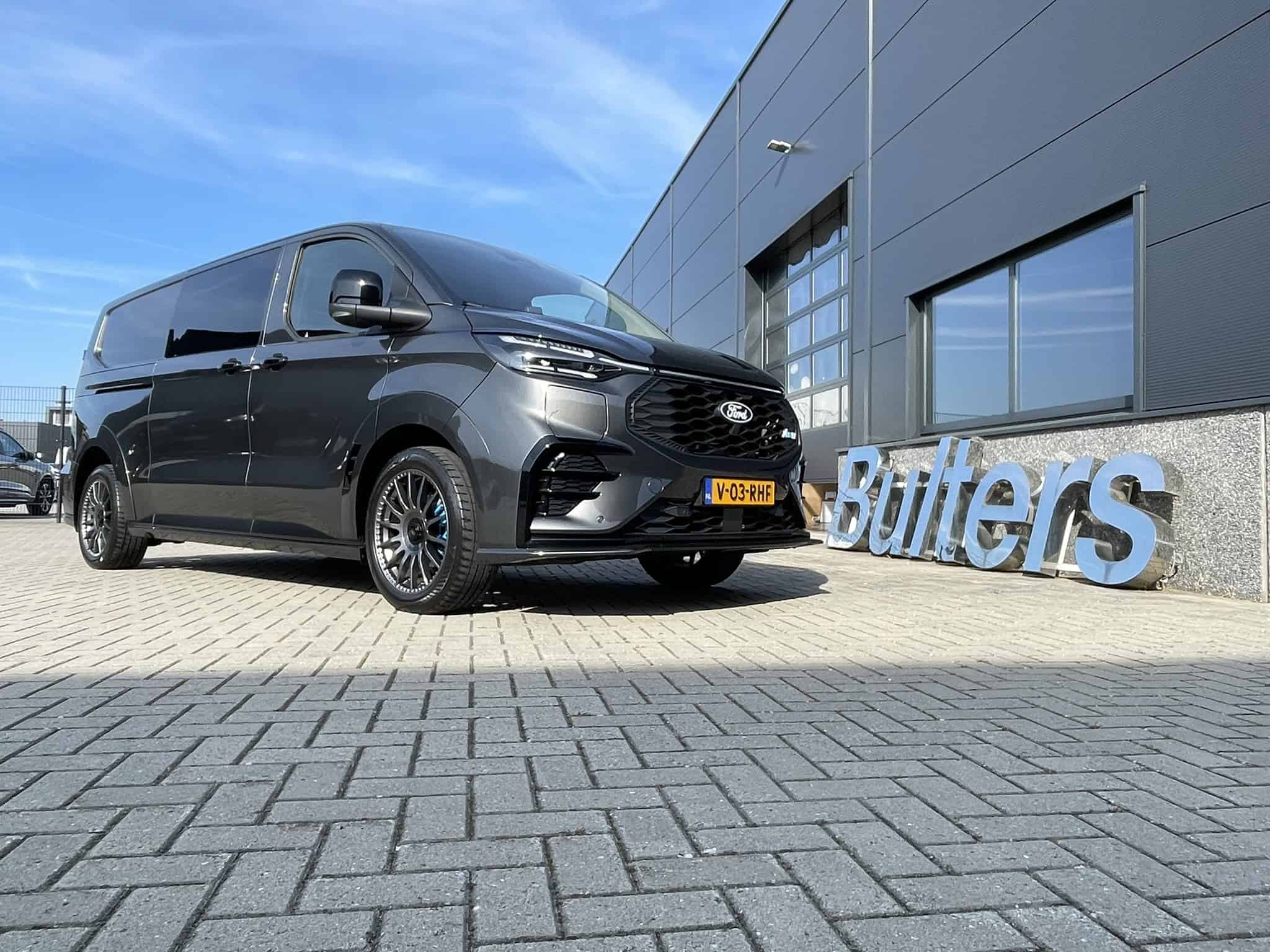 Moderne zwarte bedrijfswagen geparkeerd voor het bedrijfsgebouw met logo van Topbedrijfswagen op de achtergrond.